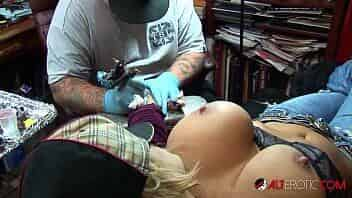 Busty blonde pornstar pulls out her huge tits while getting a tattoo on her wrist